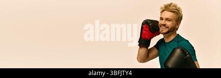 Handsome young man poses with boxing gloves, exuding confidence in a modern workout studio. Stock Photo