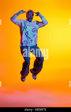 Energetic young man jumps joyfully, expressing happiness against a warm, colorful backdrop. Stock Photo