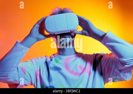 Handsome young man engages with a virtual reality headset amid an electric backdrop. Stock Photo