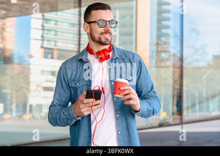Smiling man using smartphone and holding coffee cup in modern urban setting Stock Photo