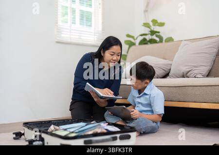 Planning and Travel. A mother showing her son a travel itinerary on a tablet while packing. Stock Photo