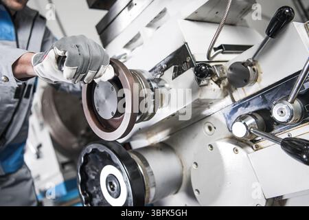 A worker skillfully manipulates a component of a machine in a factory, showcasing industrial tools and machinery. The focus is on precision and techni Stock Photo