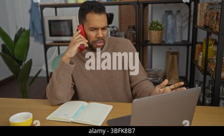 Young hispanic man in office talking on phone looking perplexed while using laptop and notebook indoors. Stock Photo