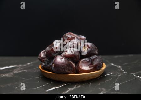 Dates fruit in wooden dish isolated on dark background. Stock Photo