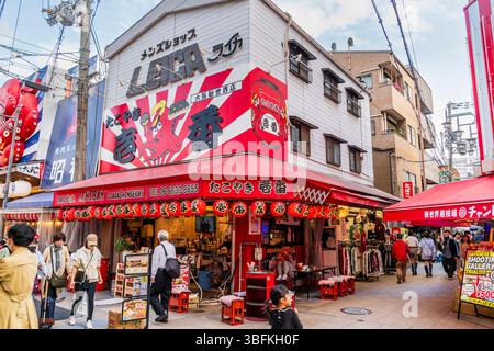 The corner Takoyaki Ichiban Osaka Sinsekaiten restaurant in Shinsekai. Large billboard with red octopus above the entrance, people walking past. Stock Photo