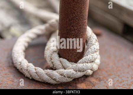 Close-up of sun-bleached rope wrapped around rusty metal bollard. The rope texture and corrosion details are clearly visible. Stock Photo