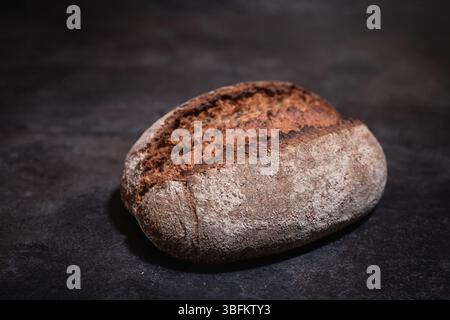 Rustic artisan bread with risen crust on dark slate background, studio shot, moody lighting, high-quality food photography Stock Photo
