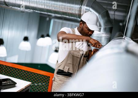 Worker performs maintenance on ventilation system in modern industrial space during daylight hours Stock Photo