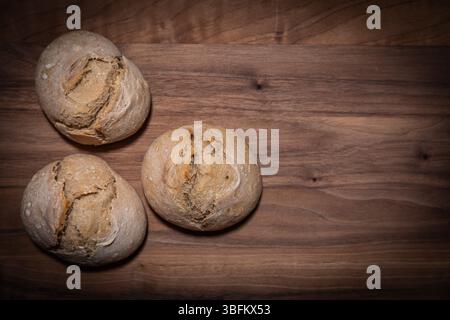 Three sourdough rolls on wooden board, placed on the left side of the image, top-down studio shot. The rest of the frame leaves space for text. Stock Photo