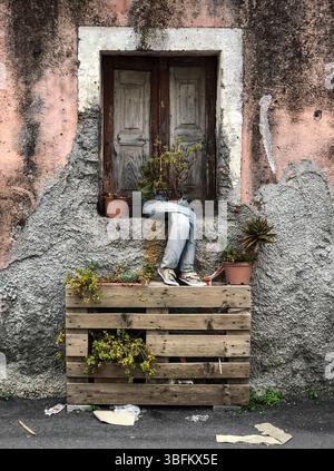 Everyday surrealism - a pair of old blue denim jeans used as a holder for plant pots in the window of an old house in Linguaglossa, Sicily, Italy Stock Photo