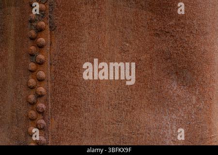 Close-up of rusty steel surface with vertical row of rivets and heavy corrosion texture Stock Photo