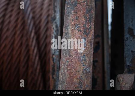 Rust-covered metal plate in focus with blurred rusty cables beside it. Industrial close-up from an abandoned Norwegian shipyard. Stock Photo