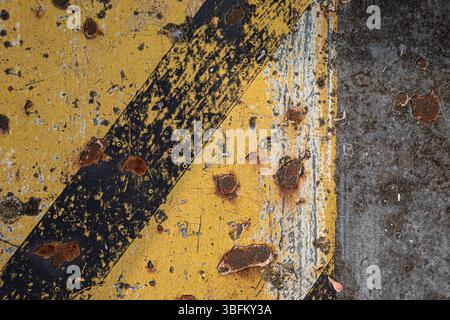Extreme close-up of rusty industrial machine part with yellow-black hazard stripes, textured metal surface showing wear and corrosion Stock Photo