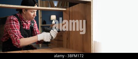 Carpentry Concept. Handyman making furniture assembly fixing cabinet installing shelf using electric drill. Banner, copy space Stock Photo