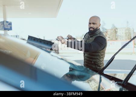 Mature man cleaning windshield of car using squeegee Stock Photo