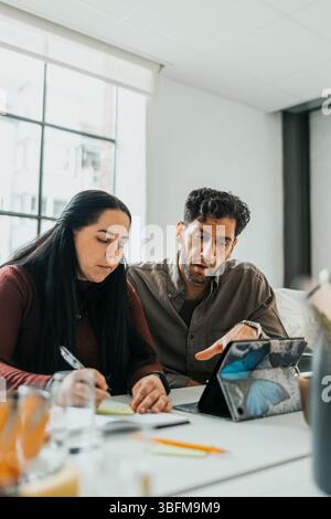 Businessman assisting female colleague writing in dairy at office Stock Photo