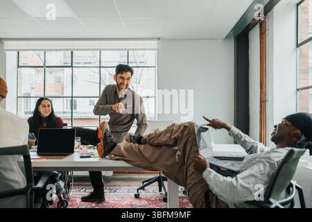 Happy colleagues laughing while pointing at each other in office Stock Photo