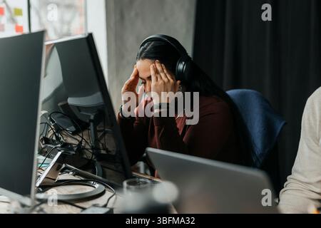 Exhausted female programmer touching temples while sitting at desk in tech start up office Stock Photo
