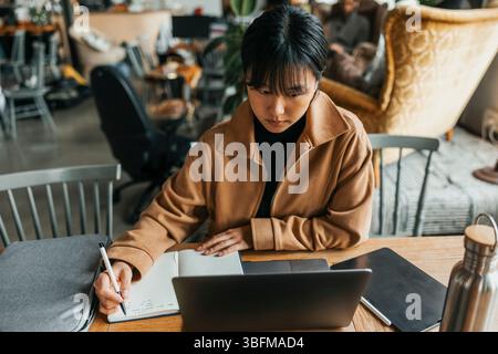 Focused young businesswoman with bangs taking down notes in diary at office Stock Photo