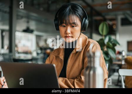 Young businesswoman with wireless headphones working on laptop at office Stock Photo