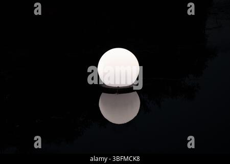 Floating round street light on water in Ukraine shines at night, an unusual solution for night lighting of a river or pond Stock Photo