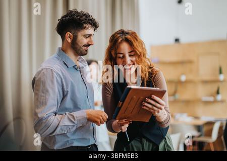 Two coworkers collaborating and laughing in a modern co working space, sharing ideas and using a tablet. Stock Photo