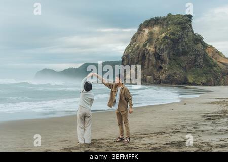 Asian tourist couple dancing together with love in Lion Rock on Piha Beach at Auckland, New Zealand Stock Photo