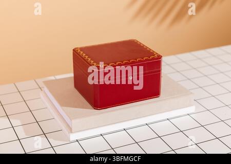 A luxurious red gift box with gold trim, elegantly placed on a stack of books, set against a modern white and black grid background with a warm-toned Stock Photo