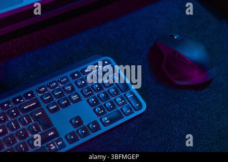 A close-up of a backlit gaming keyboard and mouse, illuminated with vibrant blue and purple LED lights, set against a dark, moody background. Highligh Stock Photo