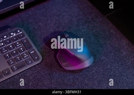 Close-up detail of a modern ergonomic computer mouse and part of a keyboard on a dark desk mat, bathed in dynamic pink and blue neon lighting. Ideal f Stock Photo