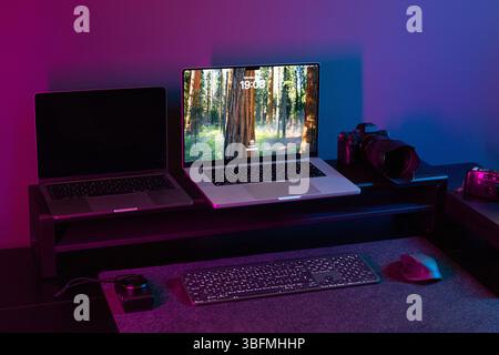 Expansive desk setup for a creative professional featuring two laptops on a riser, a professional digital camera, and a vintage camera, with a keyboar Stock Photo