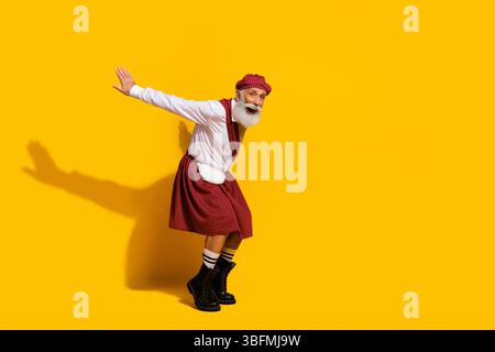 Elderly man wearing a traditional red tartan kilt playfully posing against a bold yellow background, exuding charm and style Stock Photo