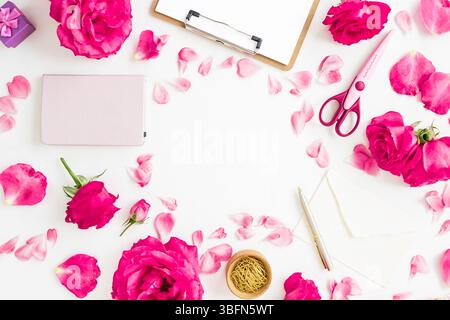 Creative workspace flat lay with pink roses, petals, notebook, scissors, and envelope on white background. Stock Photo