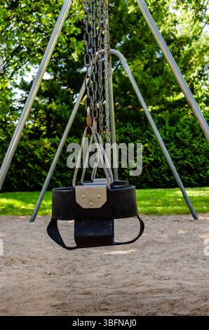 Symetrical row of child swing seats on a steel swing set in a public park play area. Stock Photo
