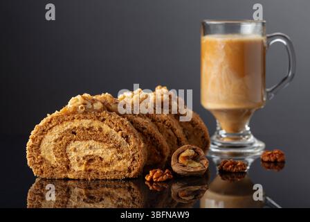 Walnut and buttercream roll: a traditional Oriental pastry. Dessert with walnuts and coffee latte on a black reflective background. Cake with brown su Stock Photo