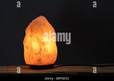 Himalayan salt lamp on wooden table with black background Stock Photo