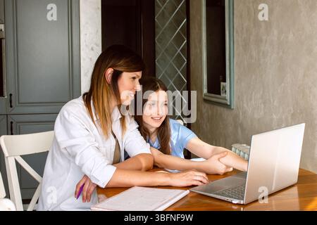 Mom and daughter surfing internet on laptop sitting in kitchen, online shopping. Watching something exciting on internet Stock Photo