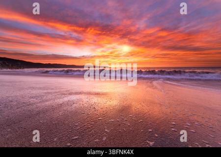 A Colorful Ocean Sunset With A Rolling Wave Breaking On Shore Stock Photo
