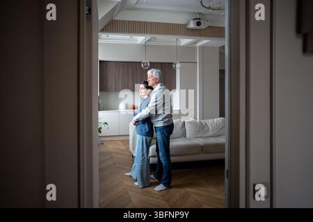 Elderly loving couple hugging looking out window. Mature romance support, aging together with trust Stock Photo