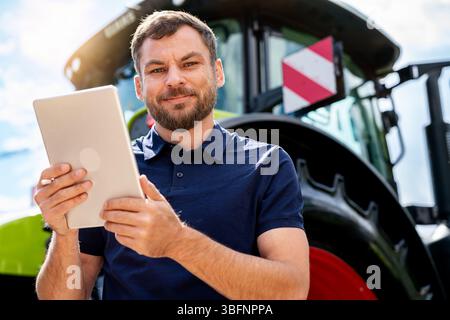 Portrait of male agribusiness professional holding digital tablet in front of tractor Stock Photo