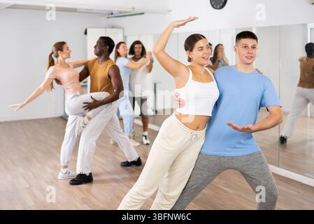 Smiling young adult couples dancing together in pairs and practicing new movements in modern studio Stock Photo
