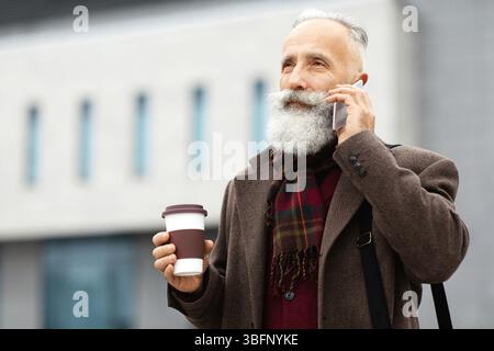 Wealthy senior man with coffee to go having business call Stock Photo