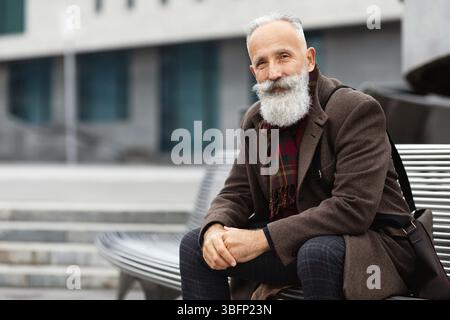 Good looking senior man sitting on bench on the street Stock Photo
