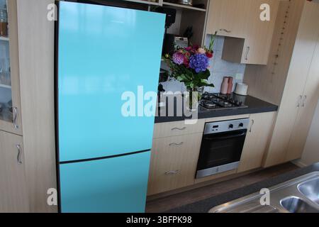 Modern kitchen with blue fridge and woodgrain cupboards and floor. Homely feeling with a bunch of flowers in a vase. Stock Photo