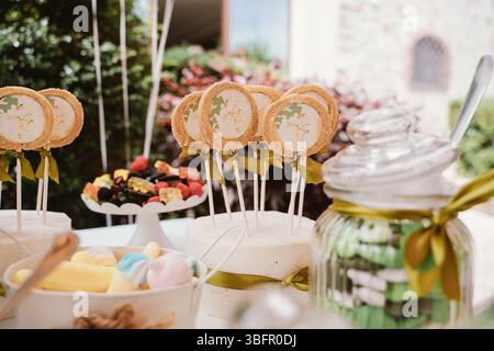 A vibrant dessert table showcasing an assortment of decorative cookies on sticks and colorful sweets in jars, perfect for a festive celebration or out Stock Photo