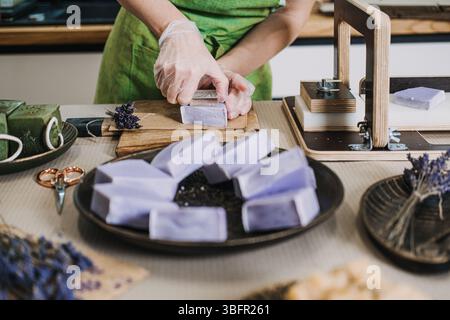 Person slices lavender soap bars by hand in a home soap studio filled with artisan tools and natural ingredients. micro business operations Stock Photo