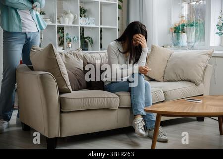 Man standing next to sad woman sitting on sofa in tense atmosphere Stock Photo
