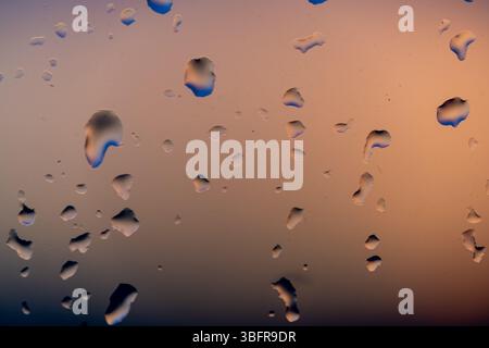 Raindrops on the window against the background of the setting sun. Background with glass and drip texture. High quality photo Stock Photo