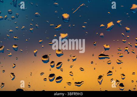 Raindrops on the window against the background of the setting sun. Background with glass and drip texture. High quality photo Stock Photo