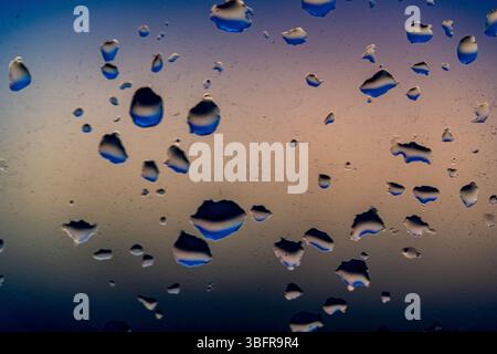 Raindrops on the window against the background of the setting sun. Background with glass and drip texture. High quality photo Stock Photo